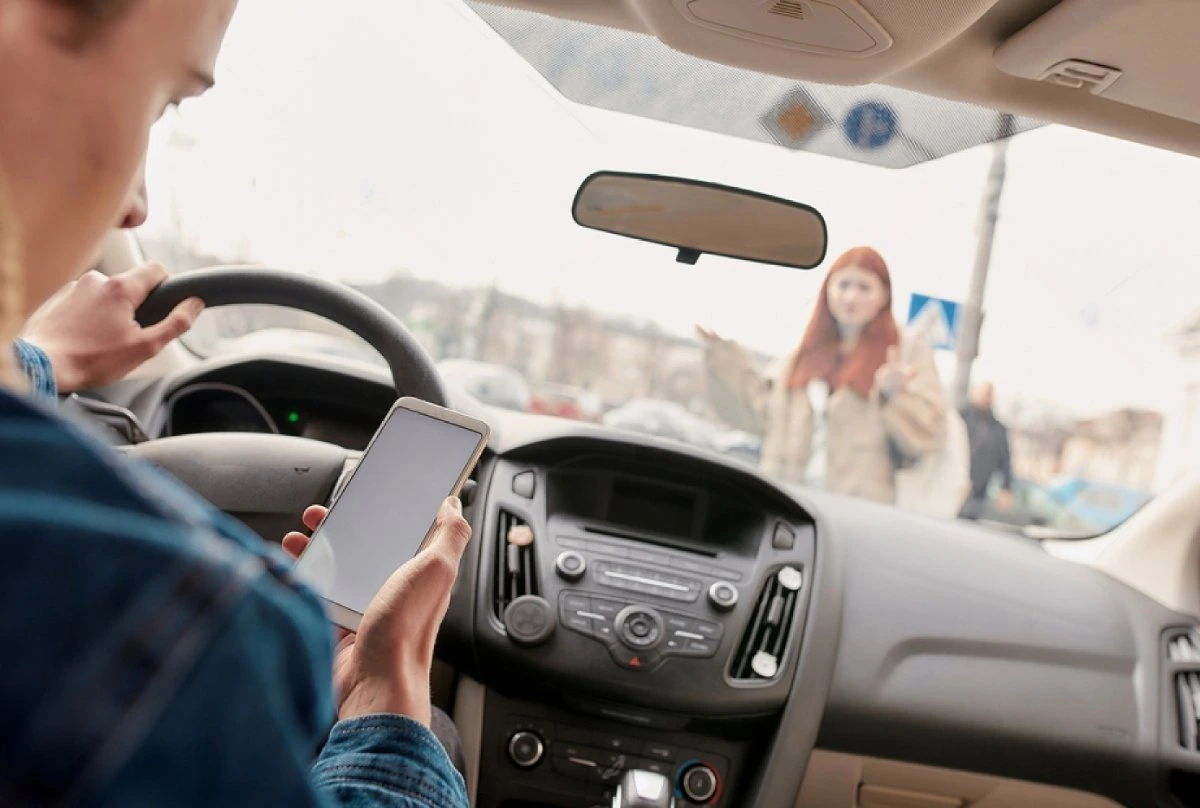 Car driver distracted by phone while driving, approaching a female pedestrian, highlighting the dangers of distracted driving.