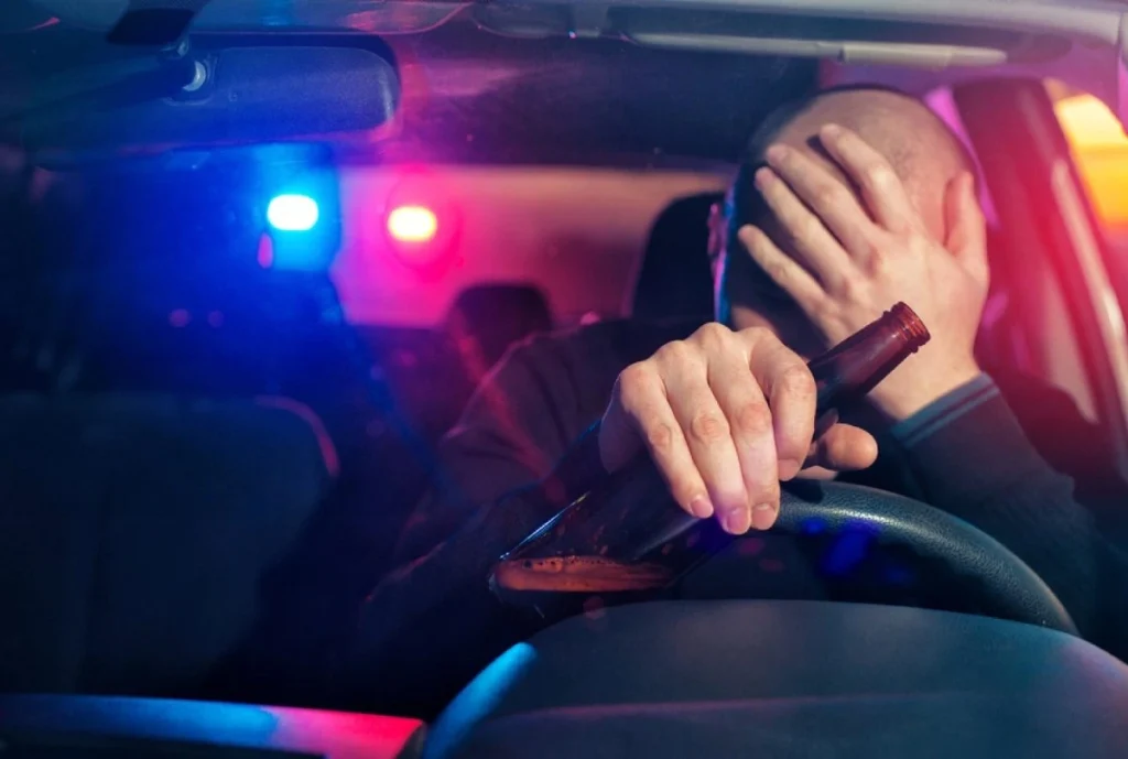 Drunk driver holding a bottle of liquor while sitting in the driver's seat, emphasizing the dangers of drunk driving.