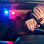 Drunk driver holding a bottle of liquor while sitting in the driver's seat, emphasizing the dangers of drunk driving.