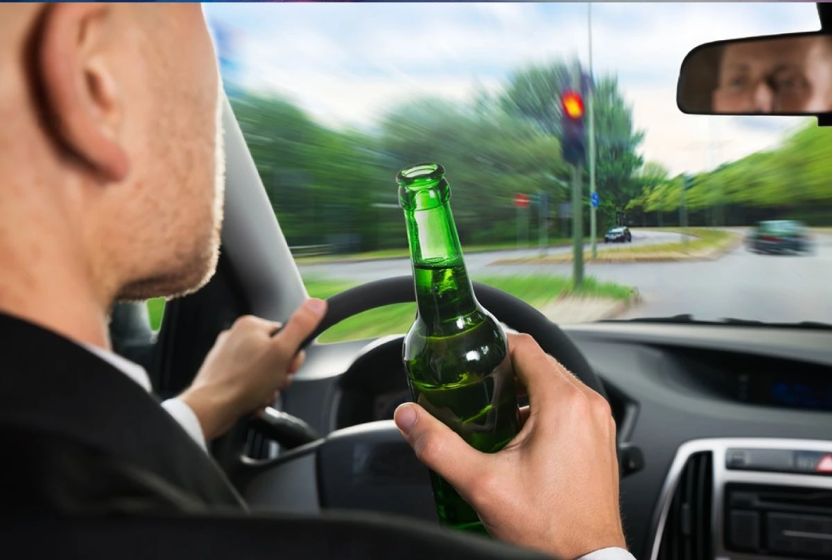 Austin Red Light Violation Accident Lawyer: Car driver holding a bottle of liquor while running a red light, highlighting the dangers of drunk driving and traffic violations.