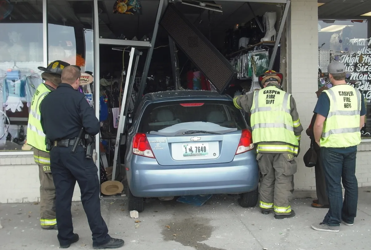 Car involved in a storefront crash with rescuers aiding and investigating the scene, relevant for personal injury claims.