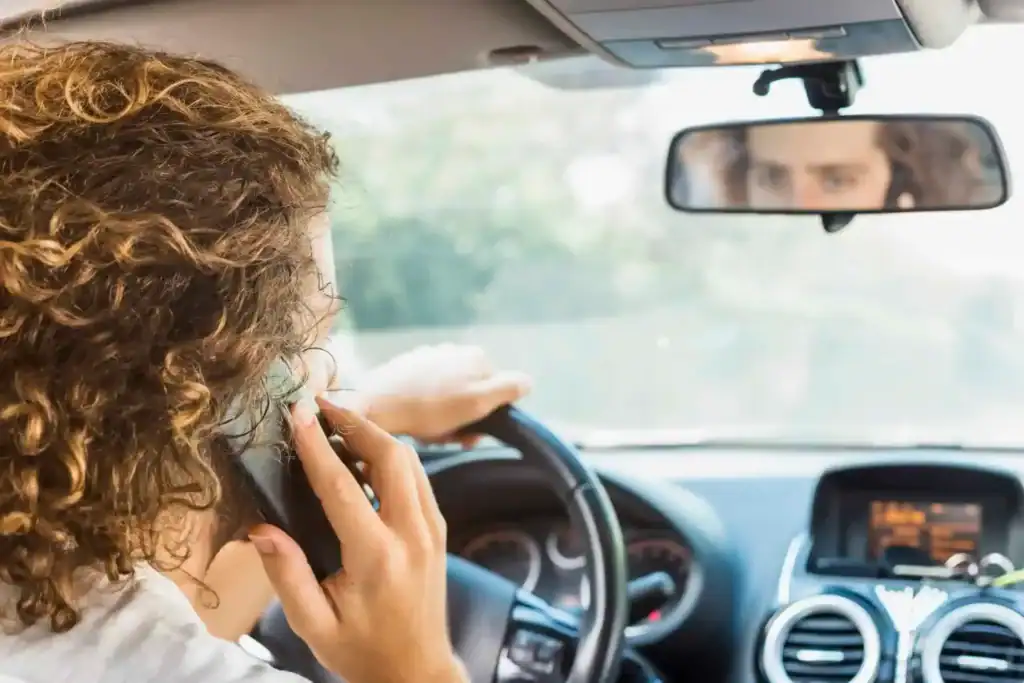 A man on phone while driving, creating accident risks on the road.